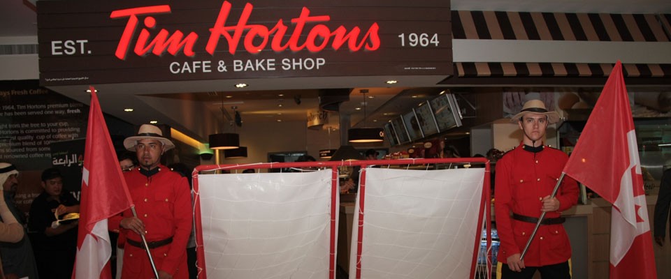 Two men wearing Canadian Guard uniform with the flags in front of Tim Hortons signboard