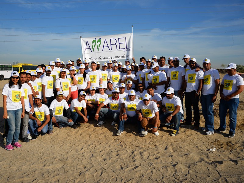 A group of people wearing t-shirts and hats with event’s logo and holding Apparel Group signboard