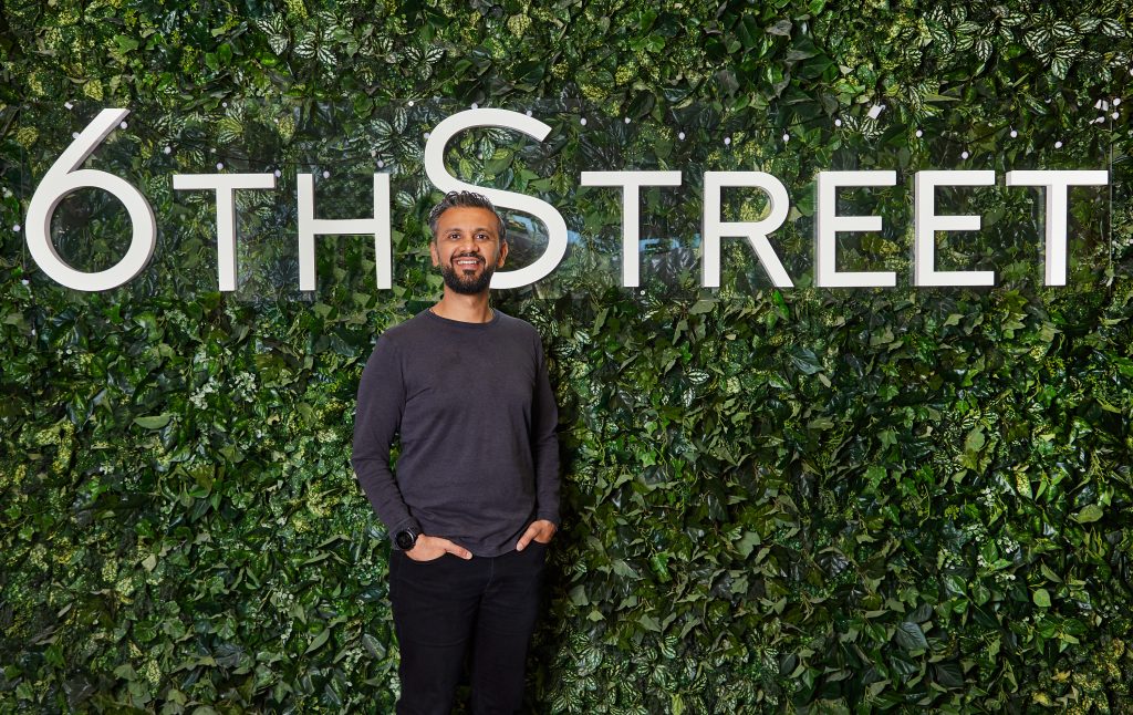 A man standing in front of 6Th Street signboard