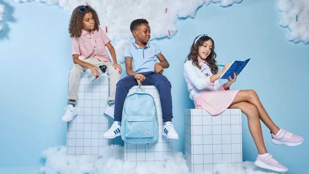 Three kids sitting on boxes among cotton clouds holding school supplies