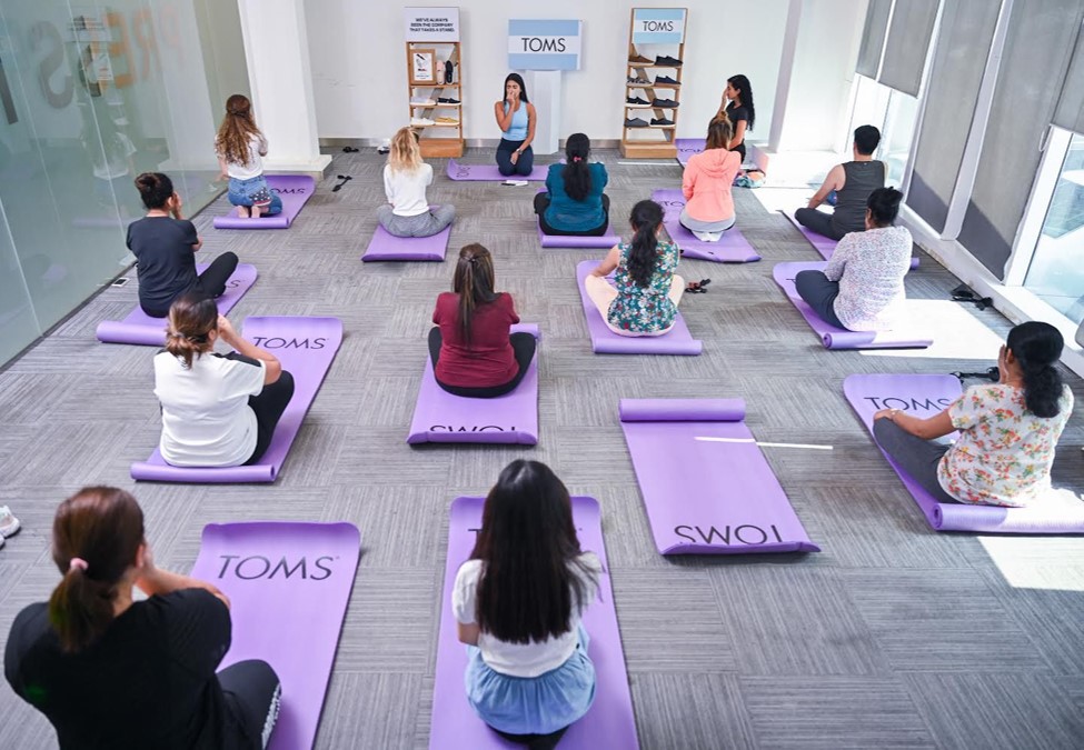 A group of women in a yoga class sitting on mats from TOMS