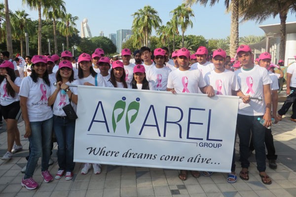 A group of people wearing white t-shirts and pink hats with breast cancer logo, holding Apparel Group signboard