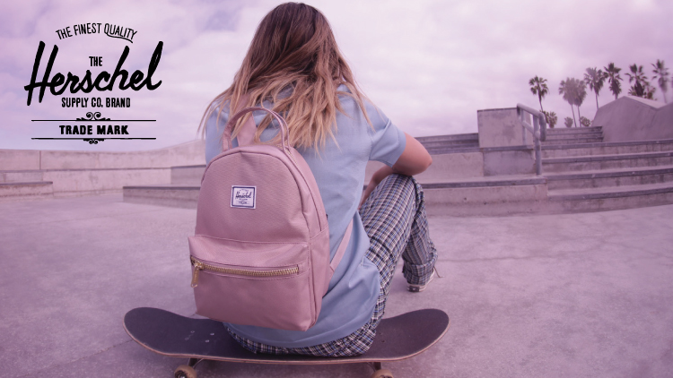 A woman sitting on a skateboard and wearing a pink bag from Herschel