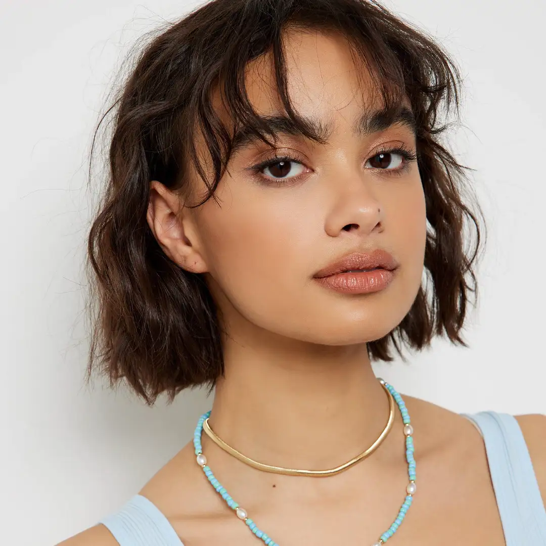 Woman wearing a blue vest top and blue and gold necklace