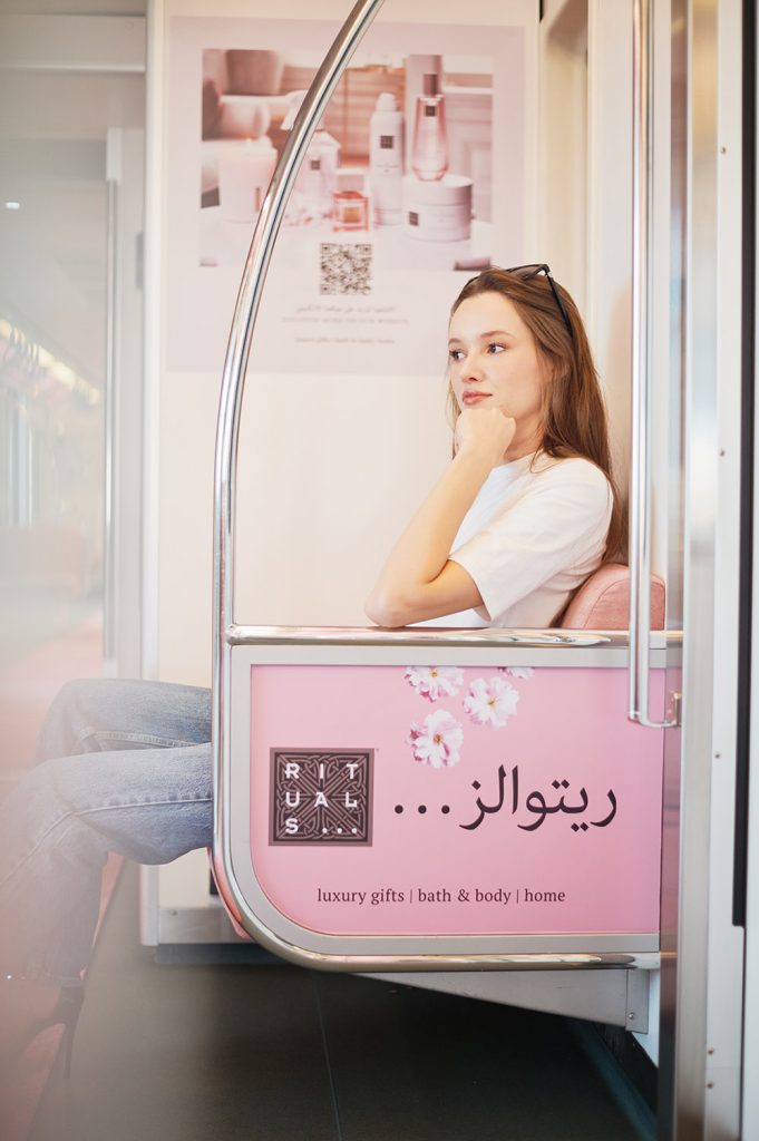 A woman sitting in the subway next to rituals ad