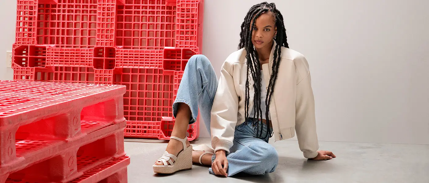 A woman wearing Steve Madden sandals next to red plastic pallets